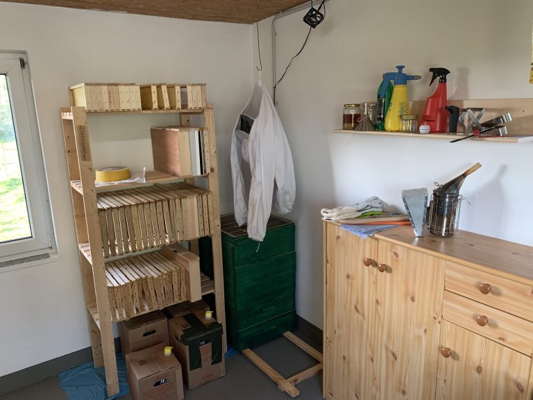 Blick ins Bienenhaus: Rähmchen-Regal, Imker-Schutzjacke und Smoker im Arbeitsraum