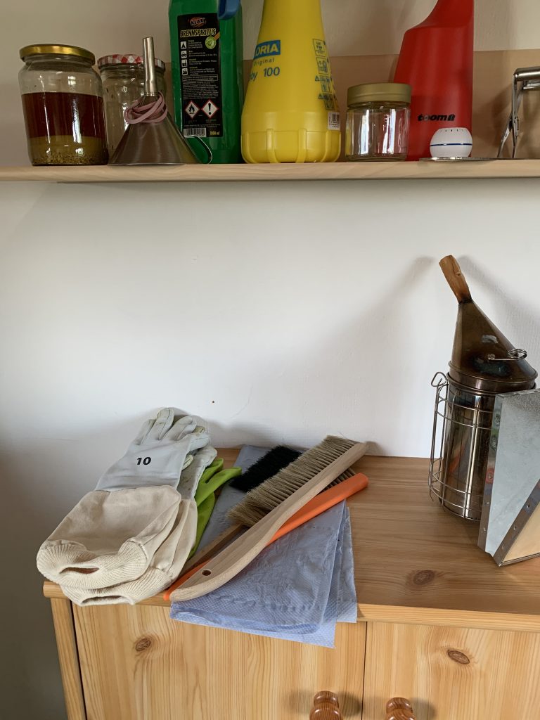 Imker-Zubehör wie Handschuhe, Bienenbesen und Smoker auf einer Kommode